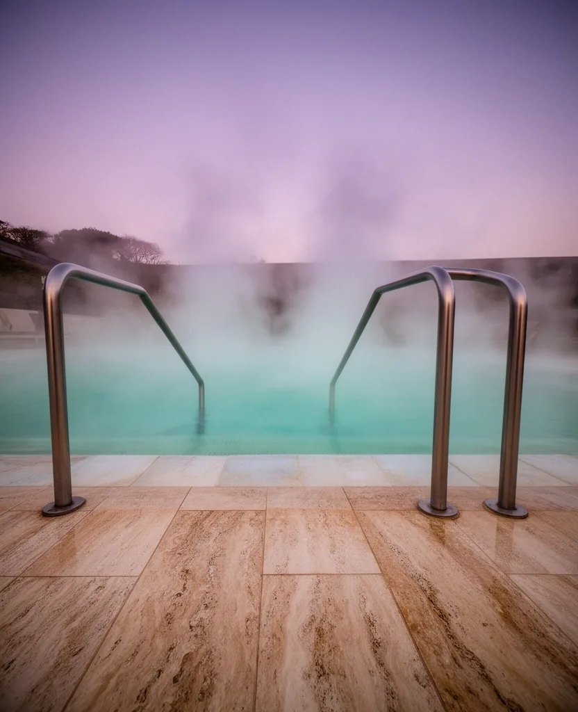 Sendero accesible hacia piscinas termales con barandas y vapor al atardecer